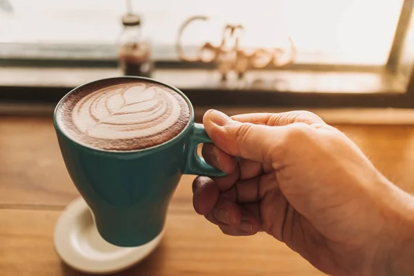 Cangkir kopi biru dengan seni latte penuh di atas meja kayu. — Stok Foto
