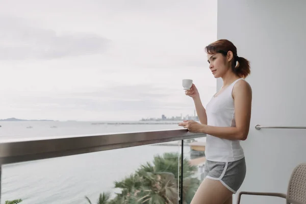 女性はコーヒーを飲み、海の景色とバルコニーでリラックスします. — ストック写真