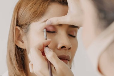 Makyaj sanatçısı müşteri gözlerine makyaj yapıyor.