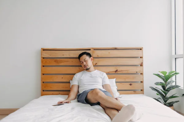 Asiático homem adormece na cama com o telefone em sua mão. — Fotografia de Stock