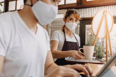 Kadın garson, yüzünde maske olan müşteriye içki servisi yapıyor..