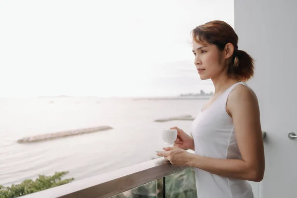 Mujer tomar café y relajarse en el balcón con vistas al mar. —  Fotos de Stock