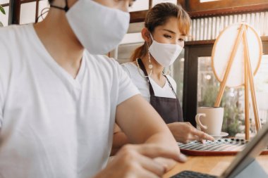 Kadın garson, yüzünde maske olan müşteriye içki servisi yapıyor..