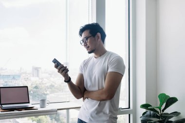 Balkon manzaralı akıllı telefon kullanan mutlu bir adam. Evden çalışma kavramı.