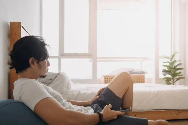 El hombre se siente relajarse y usar el teléfono inteligente en su apartamento. — Foto de Stock