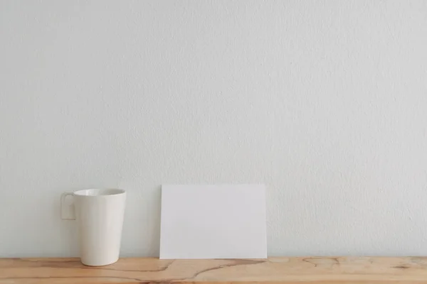 Üres fehér kártya mockup támaszkodik egy teáscsésze fehér fal. — Stock Fotó
