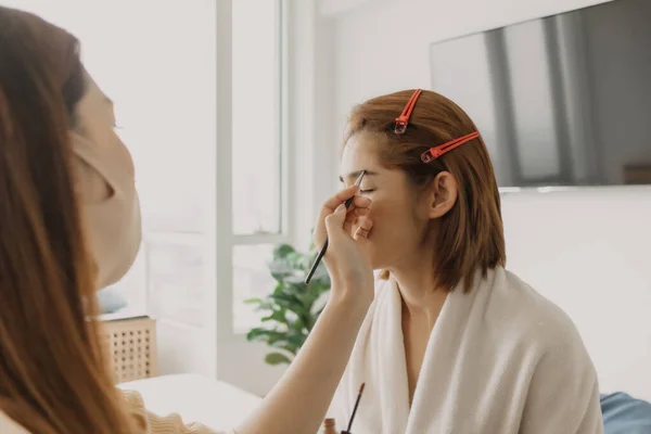 Woman makeup artist is at work and wearing makeup on her model.