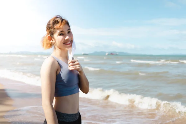 Donna togliere la maschera e riposare dopo aver finito di fare jogging in spiaggia in estate. — Foto Stock