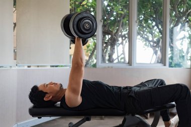 Pencere manzaralı spor salonundaki ağırlık kaldıran kaslı erkek.