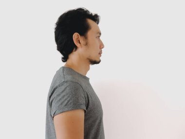 Gri tişörtlü bir adamın yan profili. Tarafsız bir geçmişe karşı düşünceli bir ifade sergiliyor..