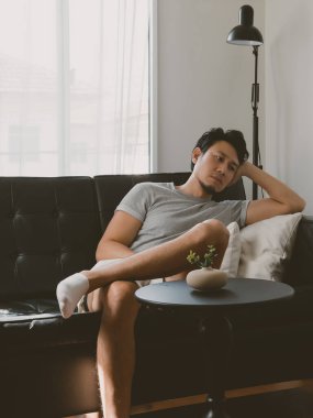 Taylandlı bir adam koyu deri bir koltuğa yaslanmış, başı yastıkta, sakin ve uykulu bir şekilde Tayland 'da sakin bir şekilde oturuyor..