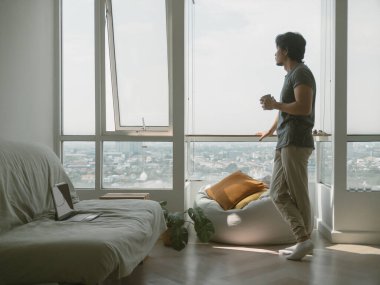 Asyalı bir adam balkonda durmuş şehir manzarasına bakıyor, iş probleminden kurtulmaya çalışıyor. Yüksek kalite fotoğraf