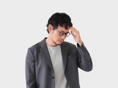 Takım elbiseli bir adam kafasına bakıyor. Gözlük takıyor ve kafası karışık ya da derin düşünceler içinde.