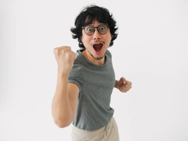 Neşeli genç bir adam neşeli bir yumrukla heyecanı ifade ediyor. Parlak, minimalist bir ortamda..