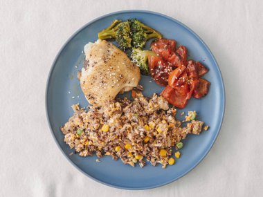 Kızarmış tavuk budu, kızarmış pilav sotelenmiş ıspanak ve kavrulmuş domatesler mavi seramik tabakta, ev tarzı sunum.