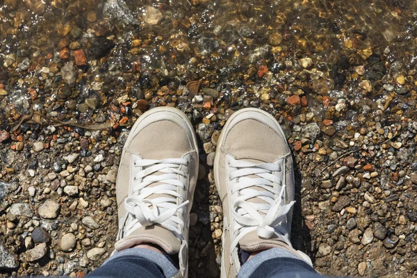 Sneakers with white laces on the feet, water and stones — Stock Photo, Image