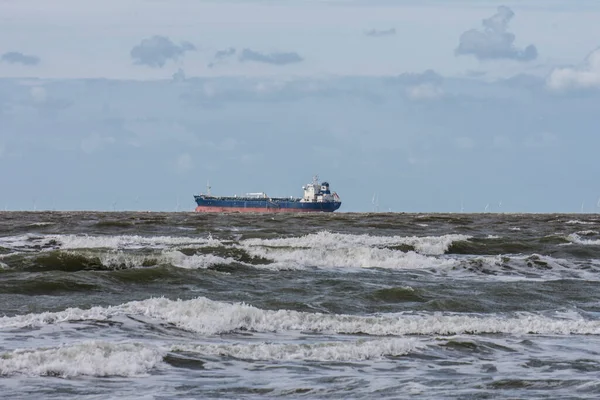 Yazın güneşli bir günde Cadzand yakınlarındaki Northsea sahilinin köpük başlarıyla dalgakıranlarda bir kargo gemisi.