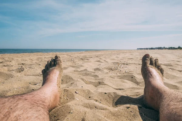 Men\'s wet feet in the sand on an empty beach in summer.