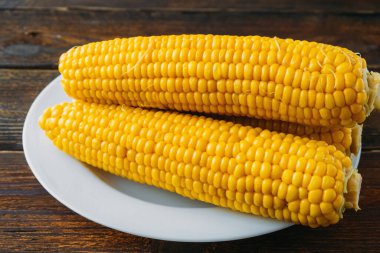 Tahtadan yapılmış ahşap bir masada beyaz bir tabakta birkaç haşlanmış mısır başı. Yukarıdan bak. Vitamin açısından zengin mısırlar.