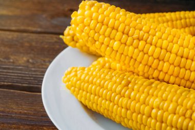 Tahta bir masada beyaz bir tabakta birkaç haşlanmış mısır başı. Yakın plan. Yukarıdan bak. Boşluğu kopyala.