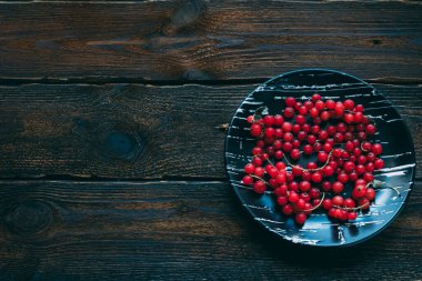 Kırsal ahşap arka planda kırmızı frenk üzümü ve seramik bir kase. Uzayı kopyala Koyu arkaplan