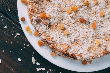 Tahta bir masada yuvarlak şekilli yulaf keki. Kuru üzüm ve mısır gevreği serpin. Köşedeki çocuk oyuncağı.