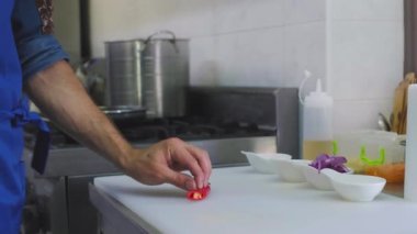 Şef, sobanın yanındaki metal bir masada, beyaz bir tahtanın üzerinde, acı kırmızı biberi halkalara ayırır ve bir tabağa koyar.