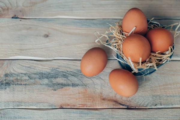 Süslü, paslanmaz çelik bir leğende, ahşap bir masada dekoratif saman üzerine tavuk yumurtası. Uzayı kopyala Metnin altına yerleştir.
