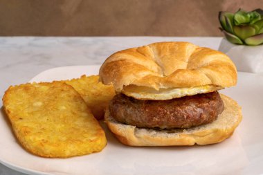   fried egg  with sausage patty  on a croissant served with hash browns