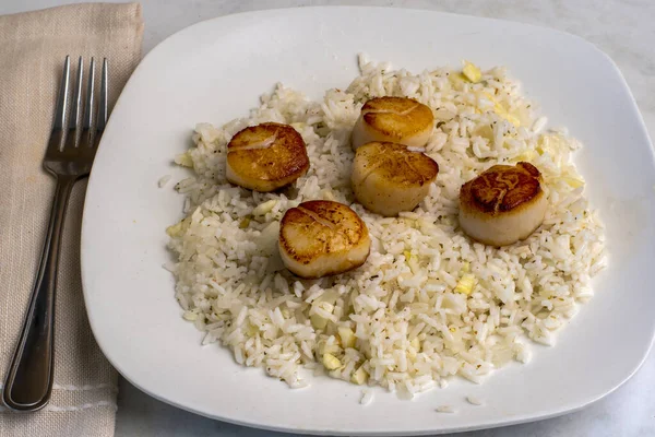 Beyaz pirinçle servis edilen tavada istiridye soğan ve sarımsak var.