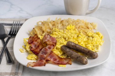 domuz pastırması ve sosis ile servis edilen çırpılmış yumurta ve kıymalı patates kızartması.