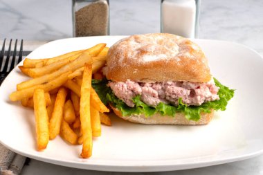 Ciabatta ekmeğine konserve jambon salatası ve marul, yanında da patates kızartması.