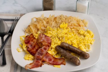domuz pastırması ve sosis ile servis edilen çırpılmış yumurta ve kıymalı patates kızartması.