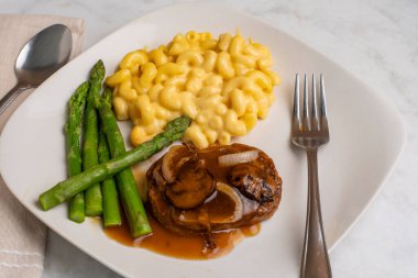 Salisbury bifteği, soğan ve mantarla birlikte kuşkonmaz, makarna ve peynir ile servis edilir.