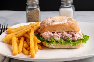 Ciabatta ekmeğine konserve jambon salatası ve marul, yanında da patates kızartması.