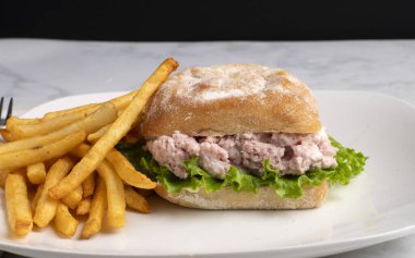 Ciabatta ekmeğine konserve jambon salatası ve marul, yanında da patates kızartması.