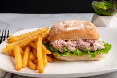 Ciabatta ekmeğine konserve jambon salatası ve marul, yanında da patates kızartması.