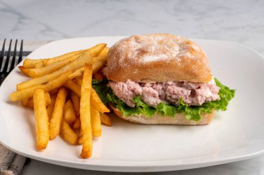 Ciabatta ekmeğine konserve jambon salatası ve marul, yanında da patates kızartması.