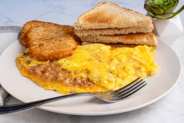 Kızarmış patates ve kızarmış ekmekle servis edilen mısır biftekli omlet.