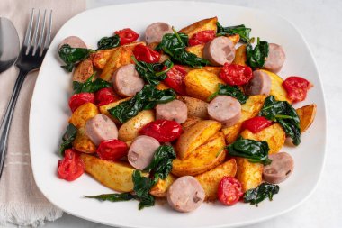 Sotelenmiş ıspanak ve domatesle servis edilmiş sosisli patates..