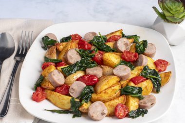 Sotelenmiş ıspanak ve domatesle servis edilmiş sosisli patates..