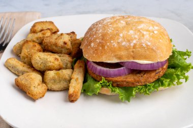 Sebzeli patates ve sebzeli patates ile servis edilen ciabatta üzerine marul ve soğanlı sebzeli burger.