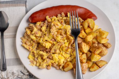 Kızarmış sosis ve ev kızartması ile servis edilen mısır bifteği ile karıştırılmış yumurta.