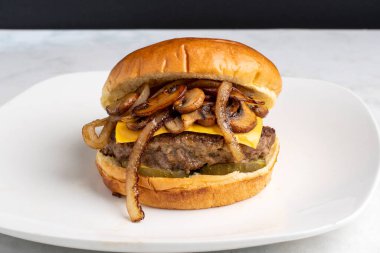 Peynirli burger turşunun üstünde sotelenmiş soğan ve biberli çöreğin üzerinde dinleniyor.