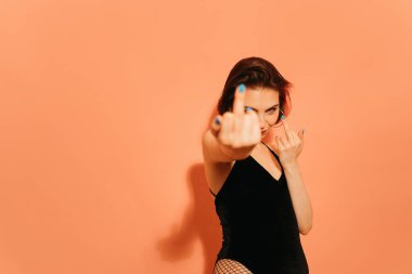 Kışkırtıcı orta parmakları olan genç bir kadın turuncu arka planda hareket ediyor.