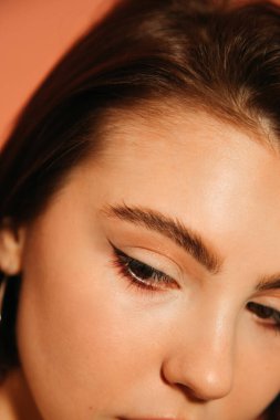 close up of young woman cropped face with shiny summer cat eyes makeup isolated on orange clipart