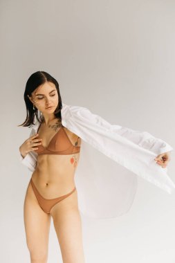 Dekoratif makyajlı, beyaz gömlekli ve arka planda bej rengi iç çamaşırlı genç bir kadın. 