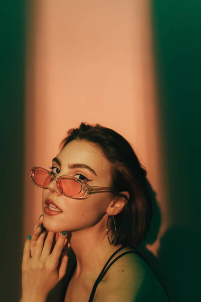 молодая женщина смотрит в камеру с полуоткрытым ртом и руками возле лица на зеленом и бежевом фоне