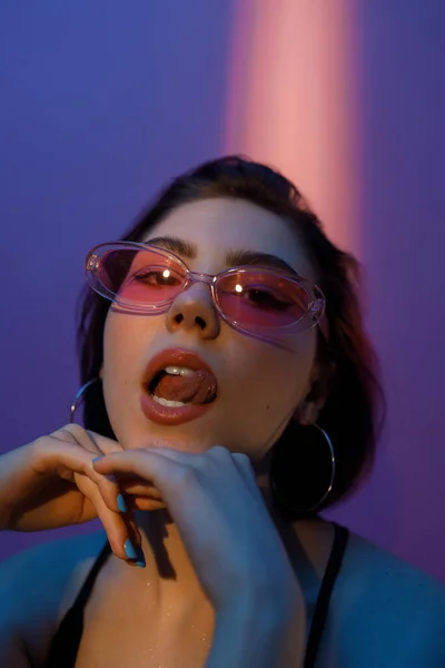 Elleri yüzüne yakın, dili menekşe ve pembe arka planda olan genç bir kadının portresi.