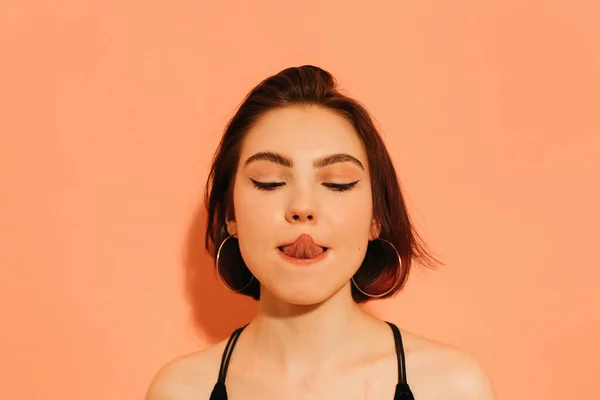 Dilini turuncu arka planda somurtan genç bir kadın.